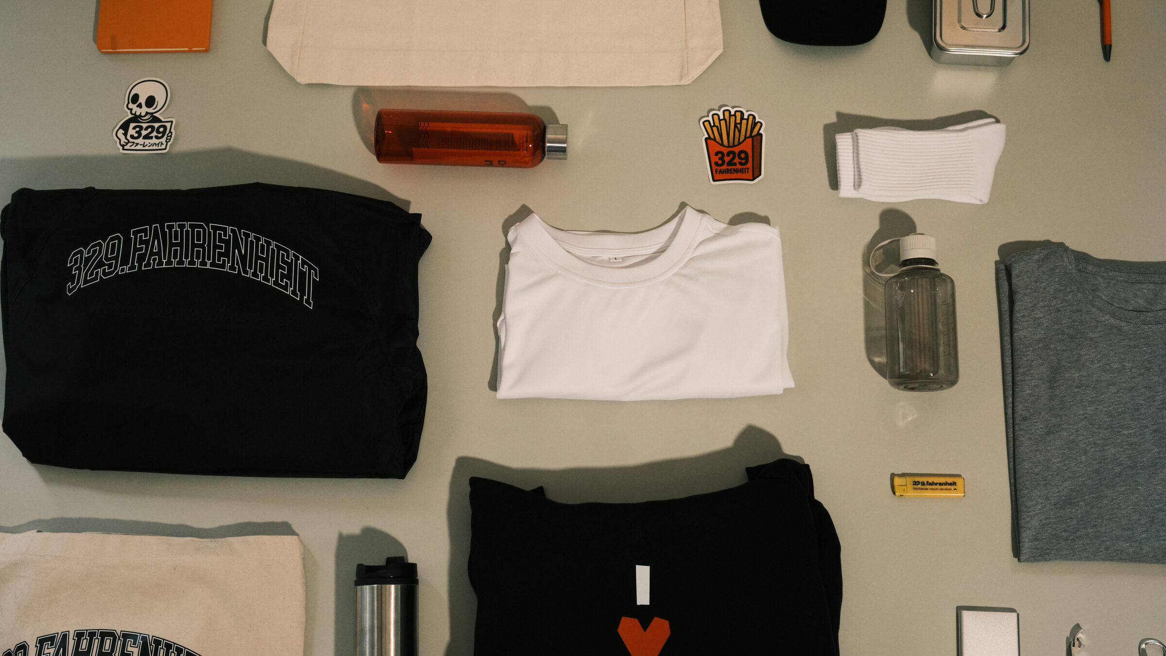 Flatlay med t-shirts, tasker, flasker og stickers fra 329